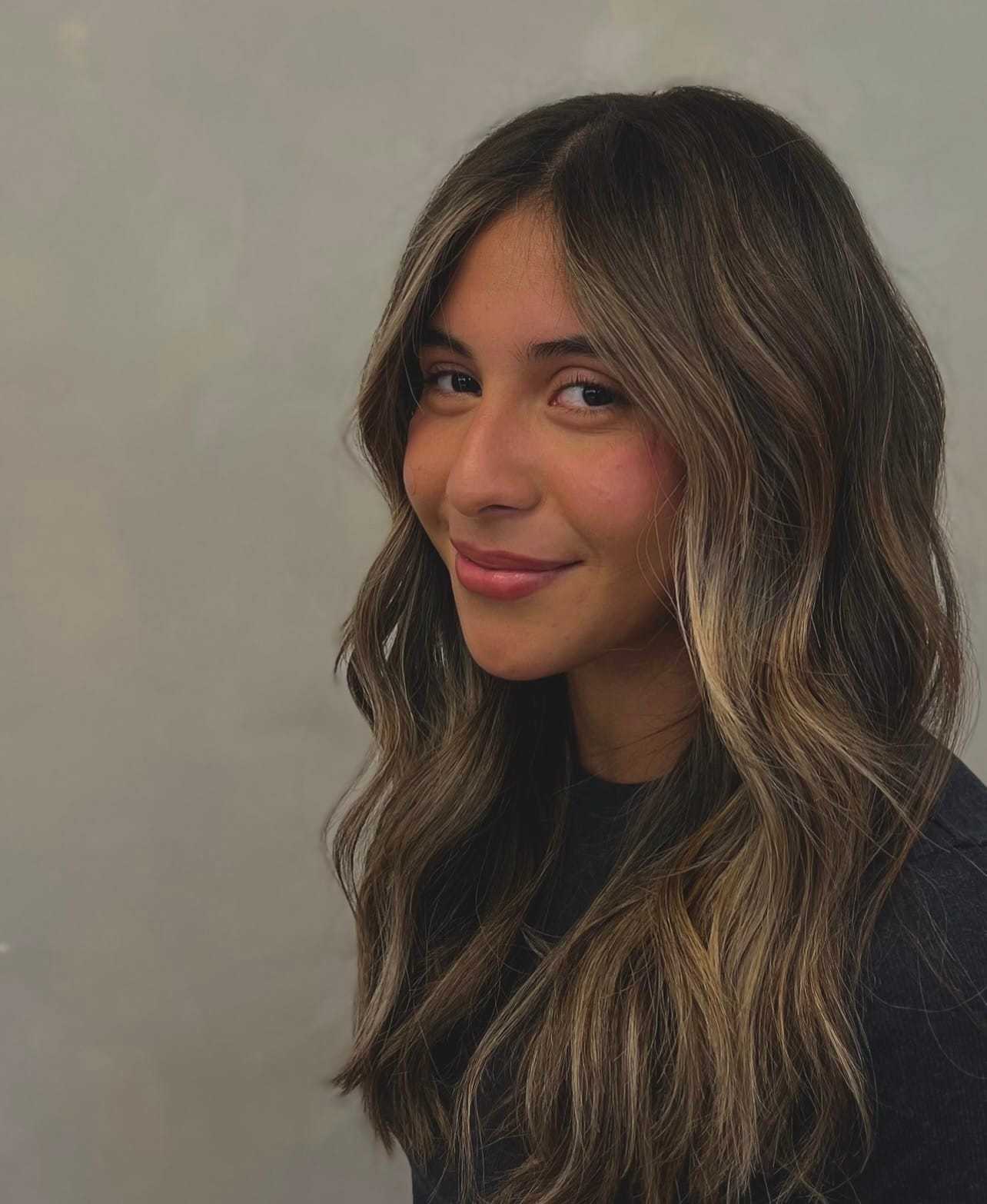 Young woman with long, wavy hair smiling gently against a neutral background.