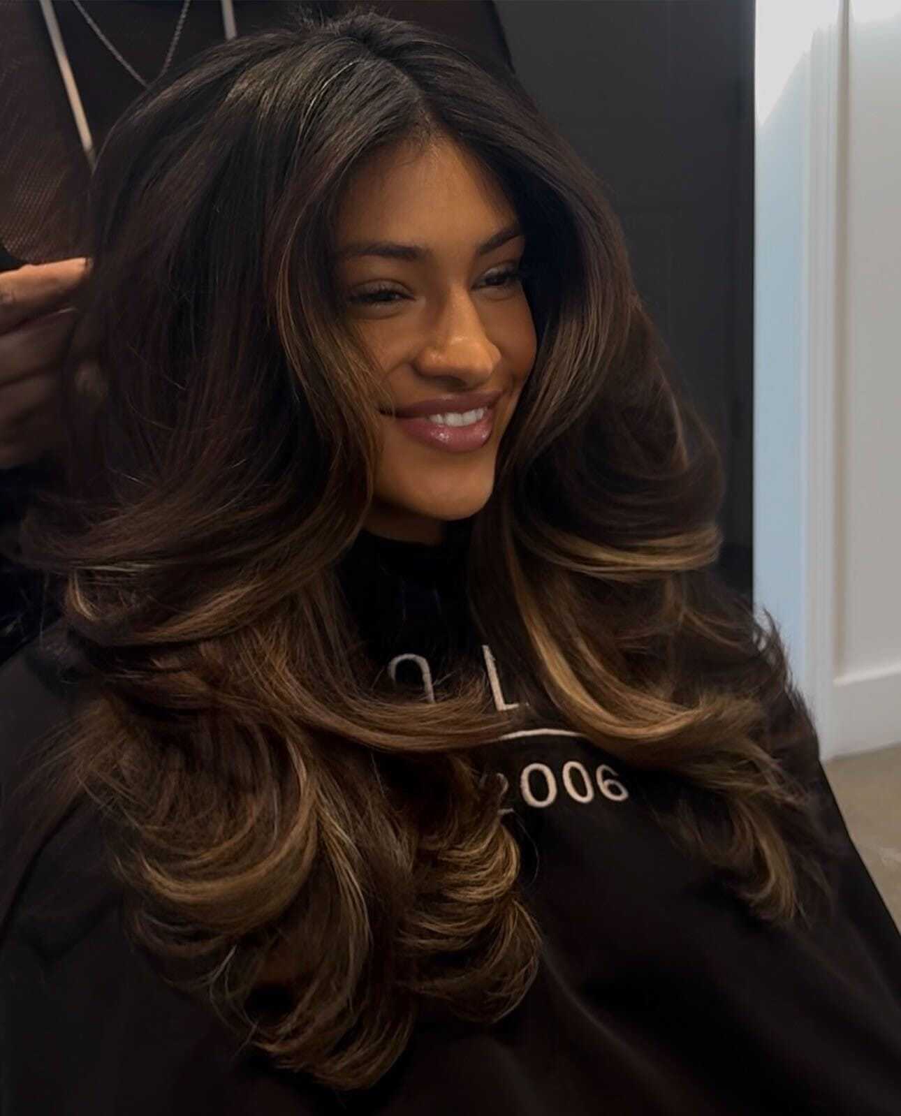 Hair stylist finishing woman's voluminous, layered hairstyle in salon.
